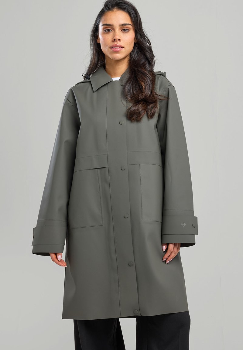 Khaki vesimproof takki, jossa on napitus edessä, suuret taskut ja leveät hihansuut. Takki on valmistettu sileästä, rakenteellisesta materiaalista ja siinä on kaulus.