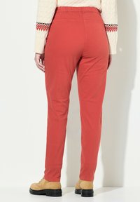 Pantalones rojos de cintura elástica con un corte ajustado, hechos de un tejido suave. Combinados con botas marrón claro, muestran la manga de un suéter de punto texturizado.