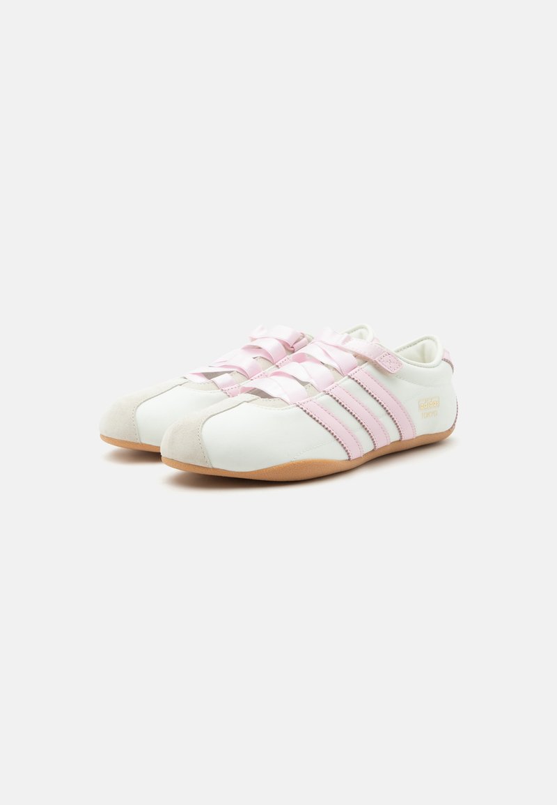 Witte en roze Adidas lage sneakers met drie strepen aan de zijkanten en lichtbruine zolen, getoond tegen een effen achtergrond.