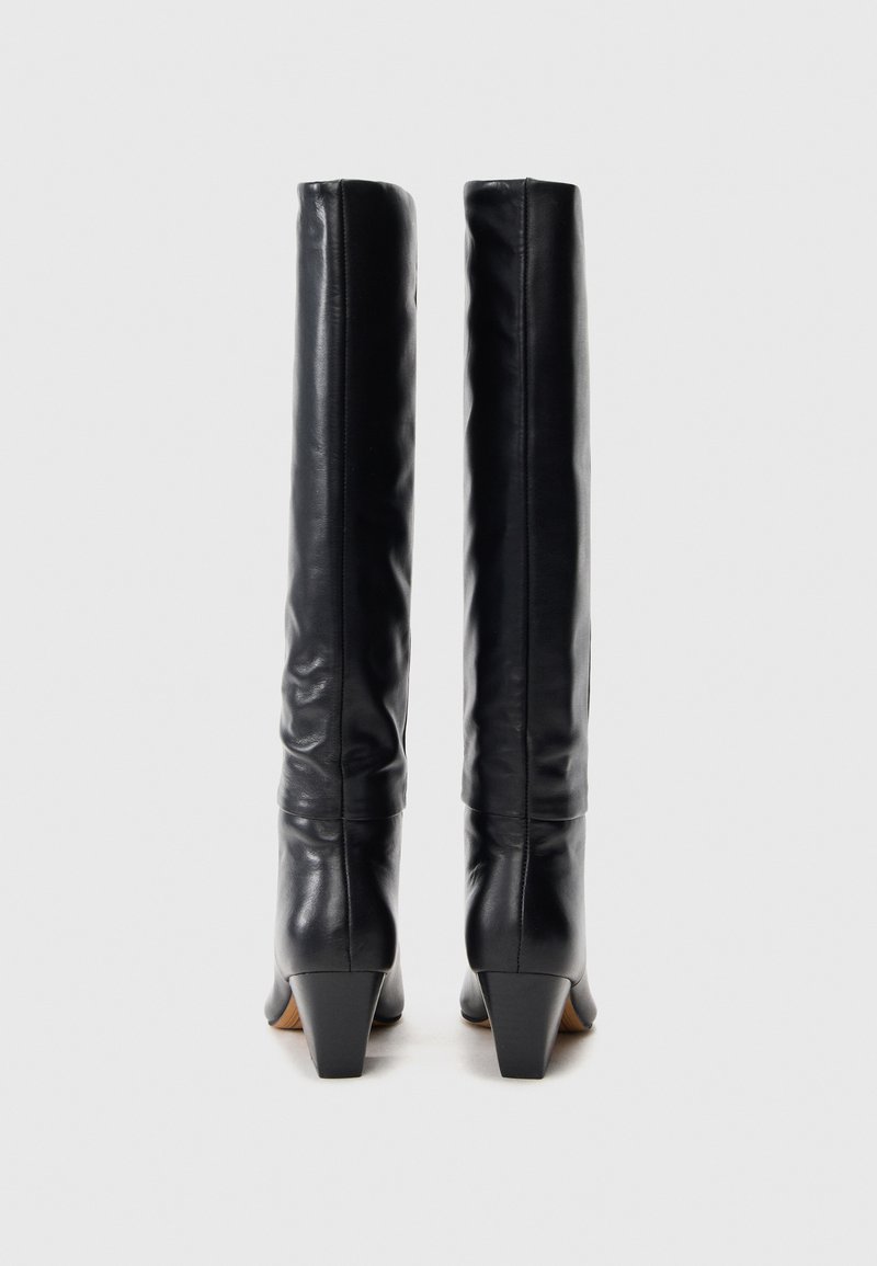 Une paire de bottes en cuir noires à talons hauts et montantes, vues de l'arrière sur un fond blanc.