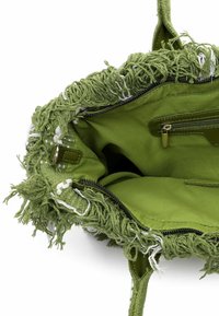 Wnętrze zielonej torby o fakturze z postrzępionymi krawędziami, kieszenią na zamek i materiałową podszewką. Charakteryzuje się żywym zielonym kolorem oraz miękkim, puszystym materiałem.