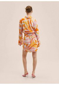 Colorful, patterned dress with long sleeves; cinched waist; features orange, pink, and yellow swirls. Paired with pink high-heeled sandals.