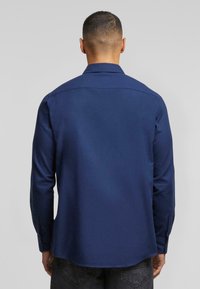 Camisa de manga larga color azul marino con cuello, puños abotonados y textura suave; sin patrones ni acentos visibles.