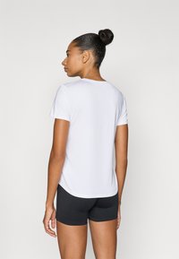 Λευκό κοντομάνικο μπλουζάκι από λείο ύφασμα, με στρογγυλή λαιμόκοψη και άνετη εφαρμογή, σε συνδυασμό με μαύρο σορτς.