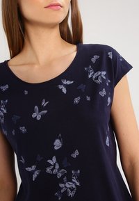 Camiseta de algodón azul marino con mangas cortas y escote redondo, que presenta un estampado de mariposas en diferentes tonos de azul.