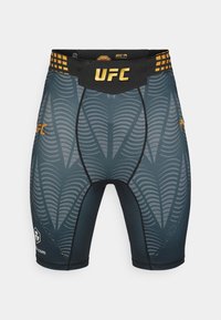 Προσαρμοσμένα σόρτς της μάρκας UFC σε σκούρο γκρι με υφή κυματιστού μοτίβου, μαύρη ζώνη μέσης με χρυσές λεπτομέρειες και επίπεδες ραφές για αντοχή.
