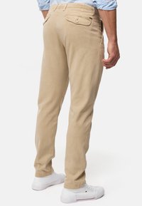 Chinos en coton beige avec une coupe slim, poches latérales et arrière, et une texture lisse. Associés à des baskets blanches dans une pose décontractée.