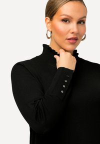 Pull noir avec un col haut à volants, design ajusté, texture côtelée et détails de boutons sur les poignets. Finition en tissu lisse.