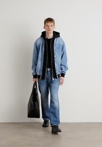 Chaqueta de mezclilla con una sudadera negra, combinada con jeans de corte amplio. Llevando un bolso tote negro. Diseño simple, estética casual.