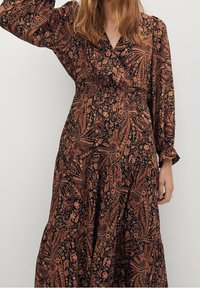 Robe longue à fleurs sombres avec des motifs paisley complexes dans des tons rouille et or. Décolleté en V, manches longues et taille froncée.