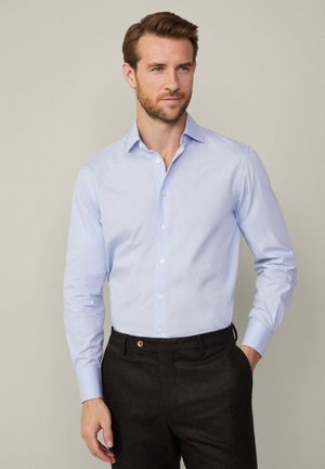 Lichtblauwe, lange mouwen button-up shirt met een gespreide kraag, voorzien van subtiele strepen. Gecombineerd met donkere broek, die een slanke pasvorm toont.