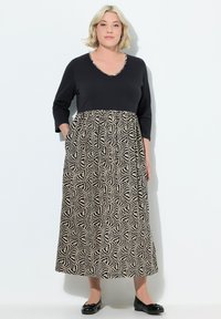 Černé a krémové šaty s třičtvrtinovými rukávy, výstřihem do V a vzorovanou sukní s geometrickými tvary. Obsahují kapsy.