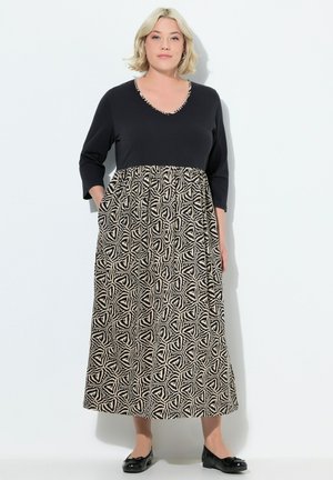Zwart en crèmekleurige jurk met driekwart mouwen, een V-hals en een patroonskirt met geometrische vormen. Inclusief zakken.
