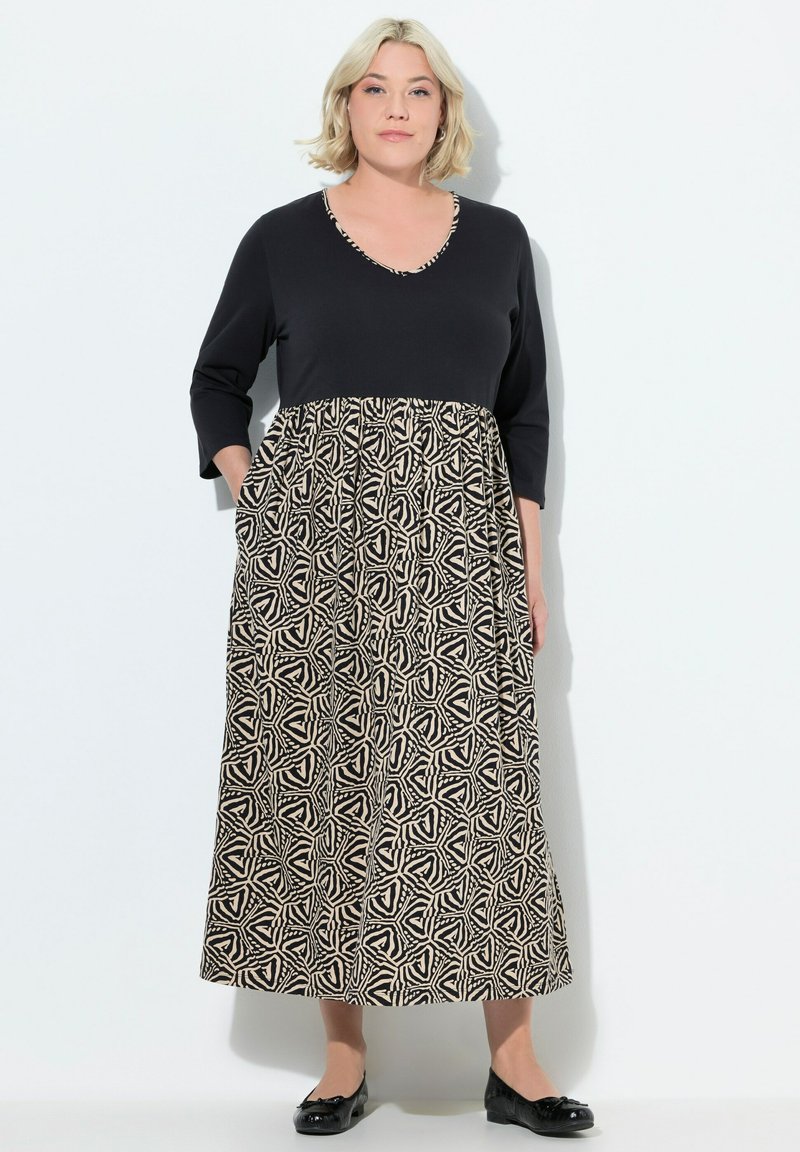 Černé a krémové šaty s třičtvrtinovými rukávy, výstřihem do V a vzorovanou sukní s geometrickými tvary. Obsahují kapsy.