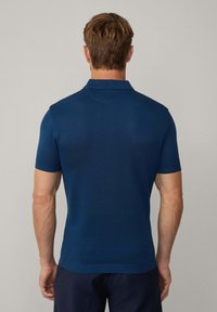 Marinblå kortärmad polo med en strukturerad stickad design, platt krage och ribbad nederkant, med en figurnära silhuett.