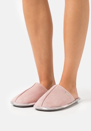 Chaussons roses doux à enfiler portés pieds nus, dotés d'un bout arrondi et d'une semelle rembourrée avec un bord gris subtil à motif.
