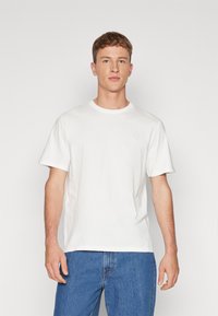 Tricou alb din bumbac, cu mânecă scurtă, decolteu rotund și un logo subtil pe piept, asortat cu blugi din denim albastru.