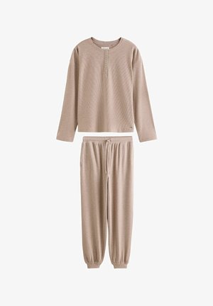 Beige top met lange mouwen met knoopsluiting en bijpassende broek met trekkoord en omslag bij de enkels, getoond op een witte achtergrond.
