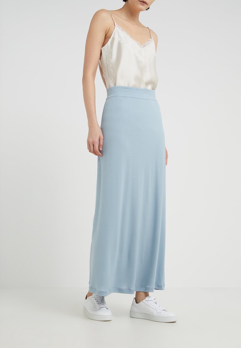 Lång blå jerseykjol med en åtsittande midja, kombinerad med en vit linne med spetsdetaljer och vita sneakers. Mjuk, slät textur.