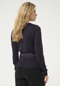 Pull en tricot bleu marine avec des fils métalliques, design ajusté, manches longues et taille texturée, vu de dos.