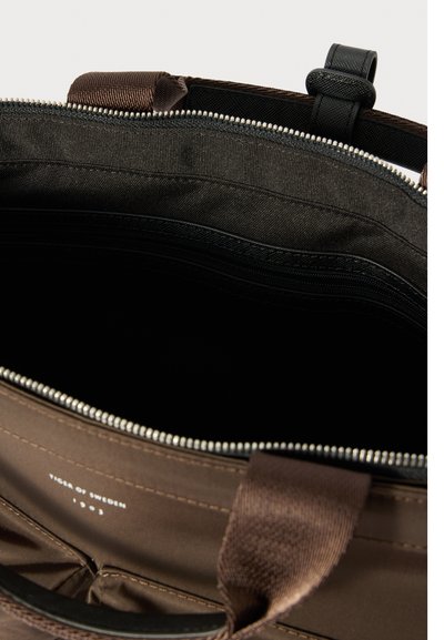 Ruda medžiaginė rankinė su užtrauktuku viršuje. Viduje yra juoda pamušalo medžiaga ir kelios kišenės. Yra siuvinėti raštai ir tvirti rankenai.