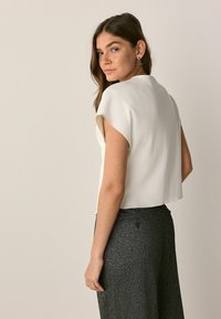 Hvid cropped top med rund halsudskæring og korte ærmer, parret med teksturerede mørkegrå brede bukser. Enkel, ren design.