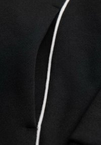 Nahaufnahme eines schwarzen Stoffkleidungsstücks mit einem Revers und einem einzigen weißen Stich, der vertikal entlang der Kante verläuft.