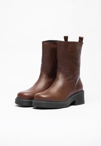 Bottines en cuir brun avec une finition lisse, semelle plateforme noire robuste, fermeture éclair sur le côté et poignées de tirage sur la tige.