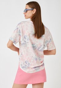 Kortærmet tie-dye t-shirt i pastelfarverne lyserød, lilla og blå. Sammen med en lyserød mini nederdel bærer modellen blå solbriller.