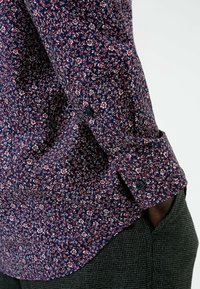 Marinblomstrad skjorta med små vita och röda blommönster, med knappad manschett och slät textur, samt grå rutiga byxor.