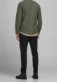 Olive green button-up shirt with long sleeves, paired with navy pinstriped trousers and black ankle boots. Simple and tailored design.