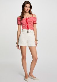 Top off-the-shoulder de rayas rojas y blancas con botones, combinado con pantalones cortos blancos de talle alto que cuentan con un cinturón. Atuendo texturizado y casual.