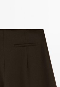 Section de jupe marron foncé sur mesure montrant une poche fendue horizontale sur un fond clair uni.