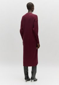 Robe longue marron bordeaux à côtes avec des manches longues et des fentes latérales, associée à des bottes stilettos noires brillantes au genou. Design simple et ajusté.