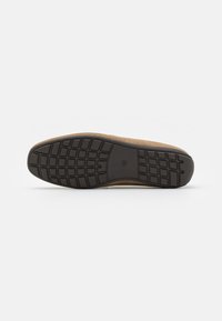 Shoe sole with a smooth brown upper and black rubber base, featuring a grid pattern for traction and flexibility.