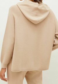 Beige capuchontrui gemaakt van zachte stof, met een losse pasvorm, raglanmouwen en een geribde zoom, met een gladde textuur.