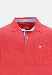 Röd pikétröja i texturerad tyg med ljusblå krage, tre-knappsslutning och en liten broderad logotyp på bröstfickan.