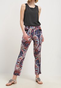 Top negro sin mangas, pantalones con estampado en navy y diseño floral, y sandalias planas de plata con embellishments.