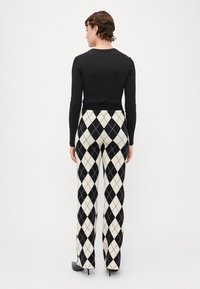 Zwarte lange mouwen top gecombineerd met hooggetailleerde, zwart-wit ruitpatroon broek. De outfit heeft een aansluitende pasvorm en hoge schoenen.