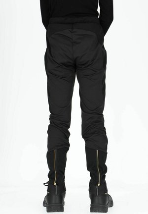 Pantaloni neri aderenti in tessuto testurizzato, con zip dorate alle caviglie e pannelli laterali a contrasto. Vista posteriore mostrata.