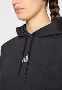 Sweatshirt preto com cordão e um logo branco discreto no peito. Tecido macio e texturizado com um ajuste confortável ao redor do pescoço.