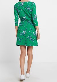 Zelené květinové šaty s kulatým výstřihem a tříčtvrtečními rukávy. Mají pás v pase a rozšířenou sukni sahající ke kolenům.