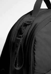 Crna torba na leđa s teksturiranom najlonskom površinom, zatvaračem na patentni zatvarač i čvrstim remenom s kopčom i dugmadi.