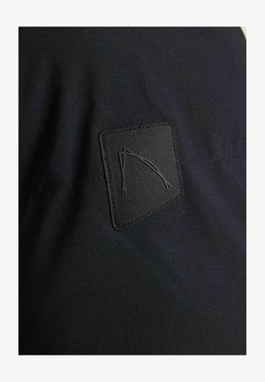 Zwart materiaal met een textuurpatch en een zwart omlijnd ontwerp. Het oppervlak is glad en iets glanzend met zichtbare stiksels.