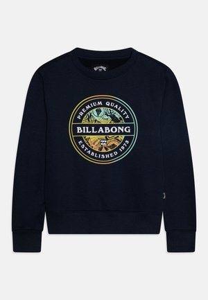 Sweat-shirt à col rond bleu marine avec logo circulaire multicolore Billabong affichant "Qualité Premium" et "Créé en 1973" sur le devant.