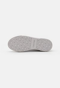 Semelle de chaussure blanche avec un motif texturé gris clair comportant le logo Calvin Klein et des motifs circulaires. Finition lisse, bords arrondis.