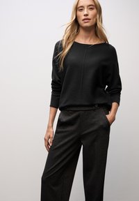 Suéter de punto negro con un escote amplio y mangas largas, combinado con pantalones de pierna ancha gris oscuro que cuentan con detalles de botones. Textura suave.