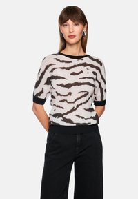 Kurzärmliger Pullover in hellbeige mit schwarzen wellenf�örmigen Streifen, ausgestattet mit einem schwarzen, gerippten Rundhalsausschnitt und Saum. Der Stoff wirkt weich und strukturiert.