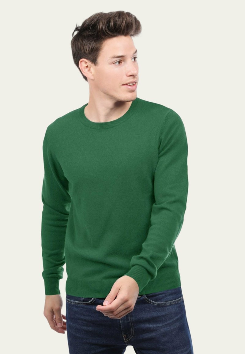 Pull en tricot vert à manches longues et col rond, avec une texture lisse et une coupe ajustée. Porté sur un jean foncé.