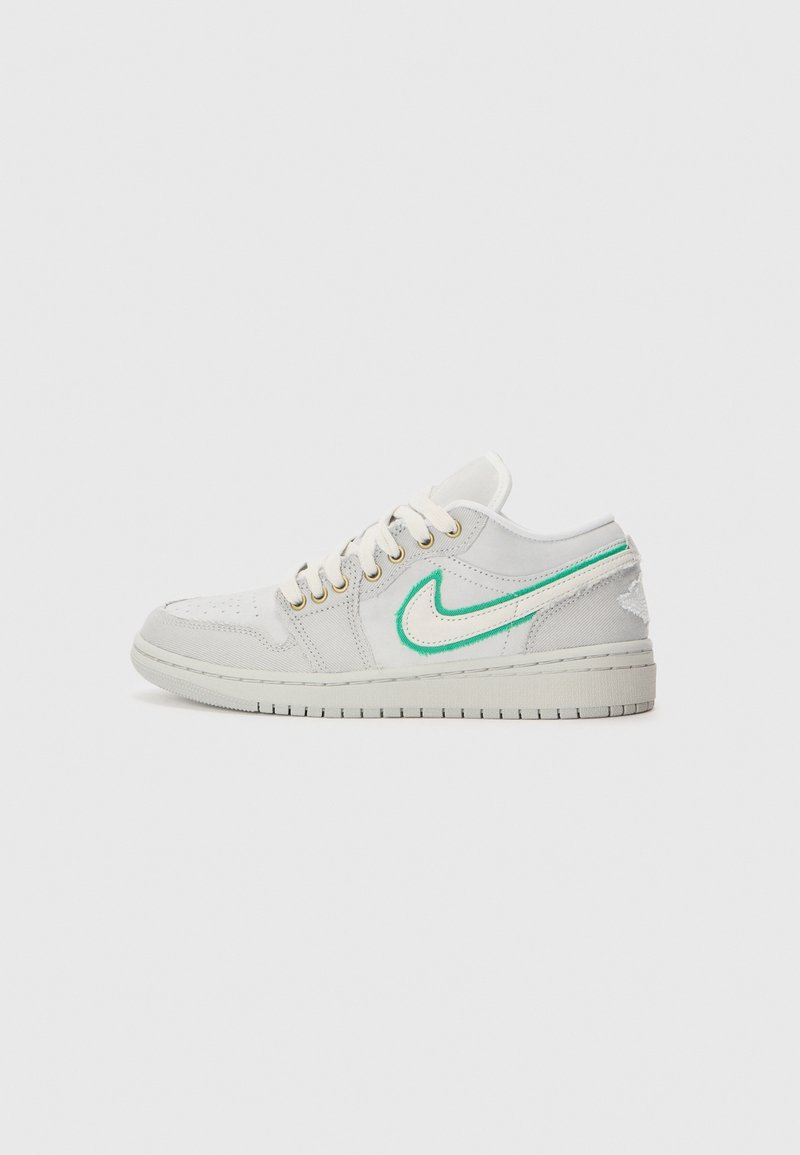 Baskets basses blanches avec le logo Nike contour vert, lacets blancs et talon légèrement usé sur un fond gris clair uni.